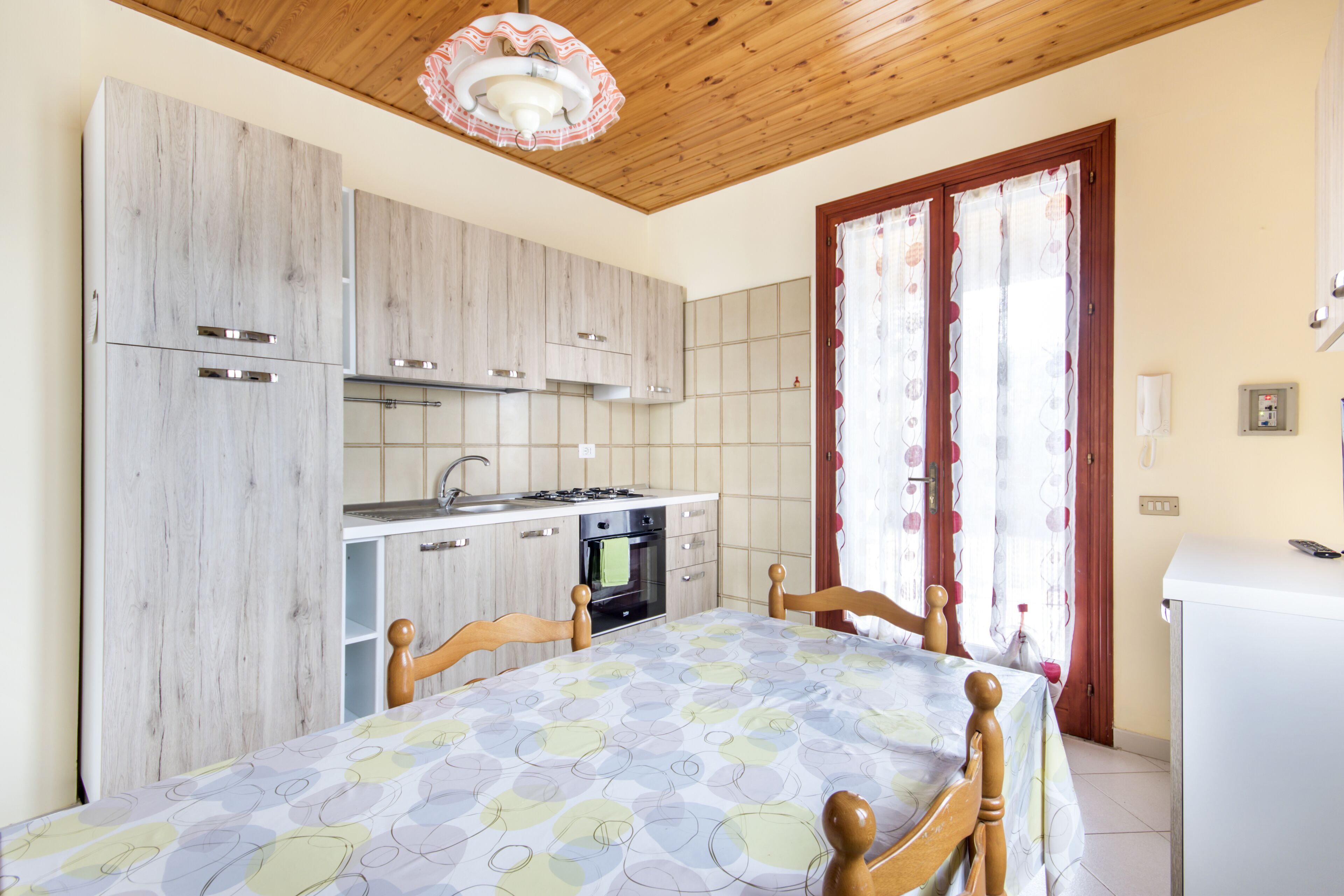 A kitchen with wooden cabinets, a dining table with chairs, and a refrigerator.
