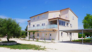Un bâtiment à deux étages doté d’un balcon, d’un espace extérieur couvert et d’une piscine en arrière-plan.