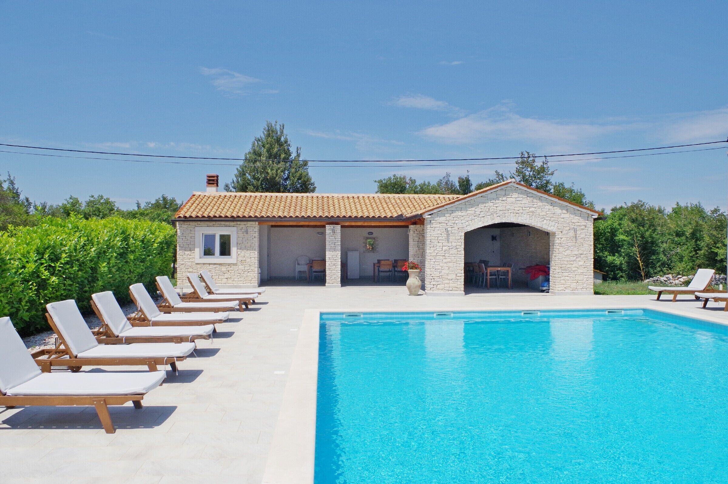 A poolside area with lounge chairs and a stone building with a tiled roof.