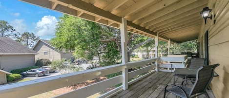 A covered porch with a wooden deck, outdoor seating, and a view of the neighborhood.