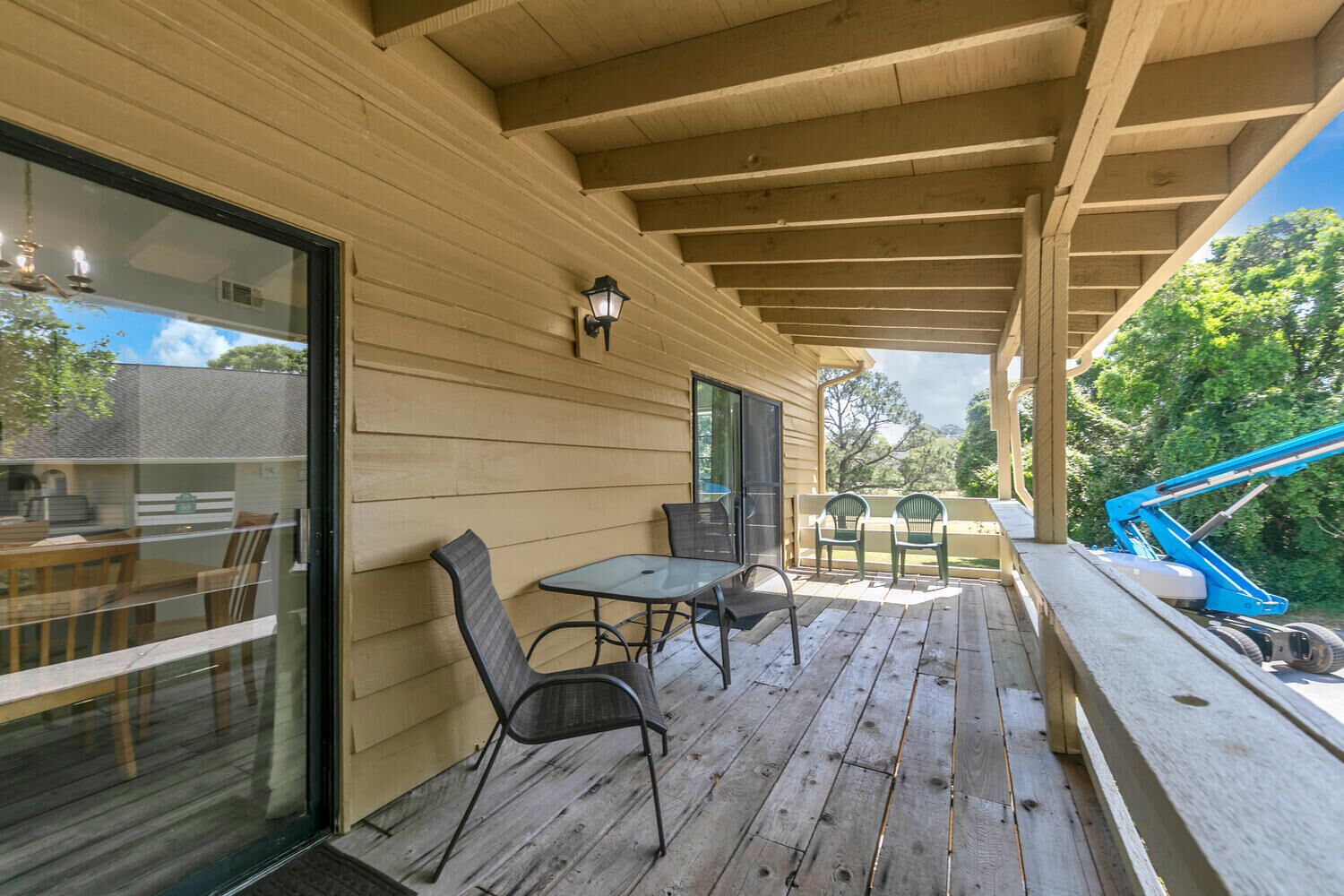 A covered patio with wooden flooring, a table with chairs, and a view of the outdoors.