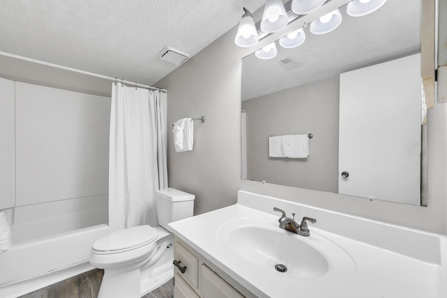 Un baño moderno con un lavamanos blanco, un inodoro, una cortina de ducha y un espejo grande.