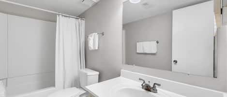 Un baño moderno con un lavamanos blanco, un inodoro, una cortina de ducha y un espejo grande.