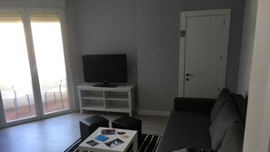 A living room with a sofa, a coffee table with magazines, a television on a stand, and a door. - Hostal I Dream Salamanca (Salamanca)