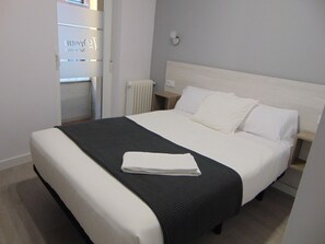 A neatly made bed with white linens and a black throw blanket, a bedside table with a lamp, and a radiator on the wall. - Hostal I Dream Salamanca (Salamanca)