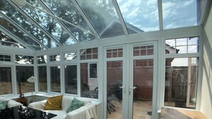 Une véranda dotée d’un toit en verre, de portes à cadre blanc et offrant une vue sur le jardin arrière.