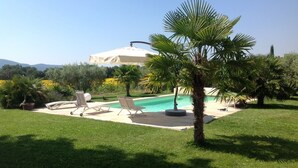 Ein Poolbereich mit Liegestühlen, einer Palme und einem Gebäude im Hintergrund.