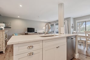A modern kitchen with a central island, built-in dishwasher, and a dining area with a wooden table and chairs.