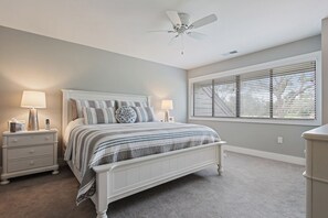 A bedroom with a bed, nightstands, a ceiling fan, and a window with blinds.