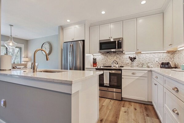 A modern kitchen with white cabinetry, stainless steel appliances, and a marble countertop.