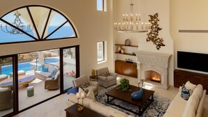 Ein geräumiges Wohnzimmer mit Kamin, großem Fernseher und Meerblick durch ein halbrundes Fenster.