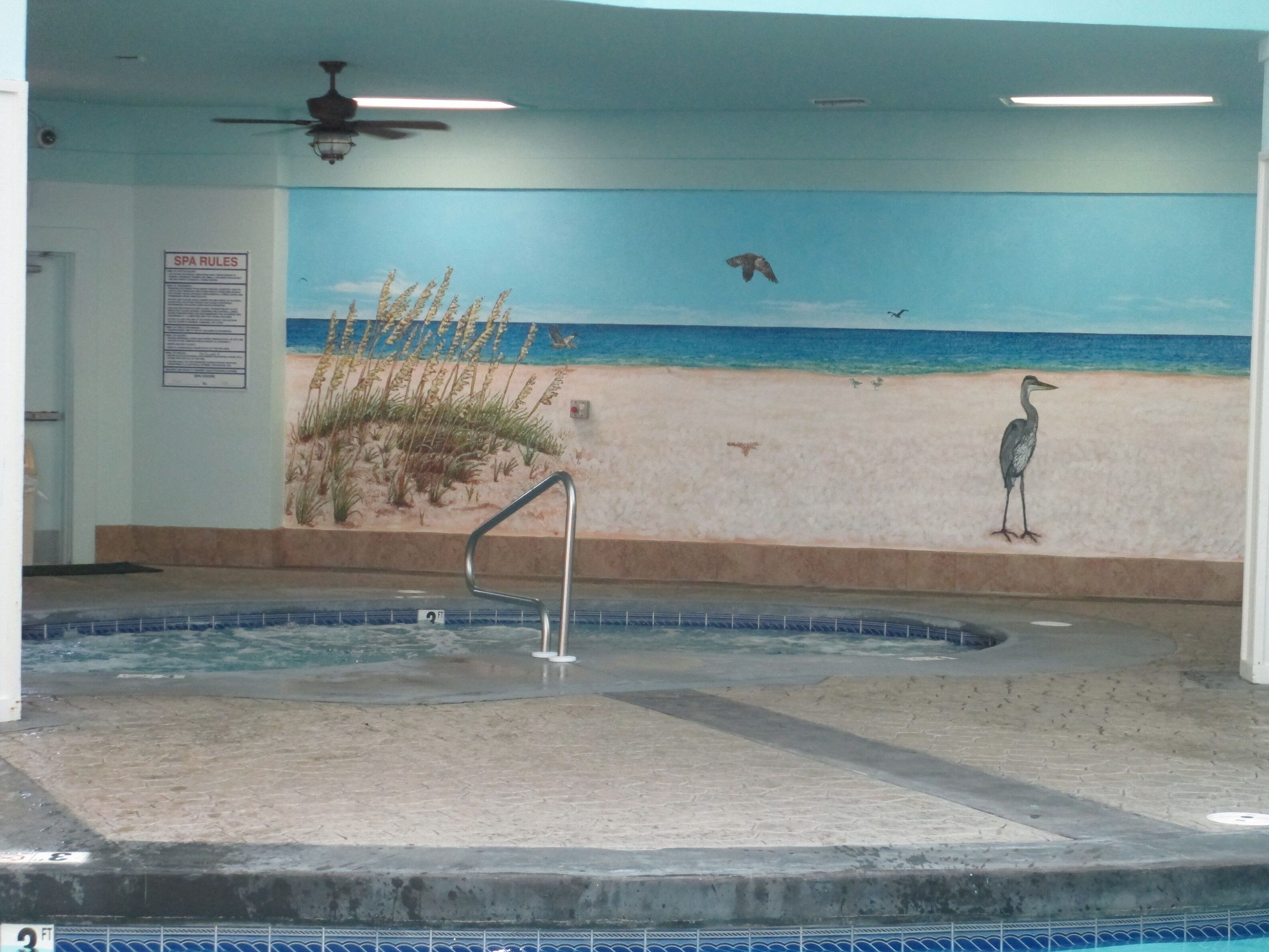 Zona de spa con un mural de una playa, una bañera de hidromasaje y un ventilador de techo.