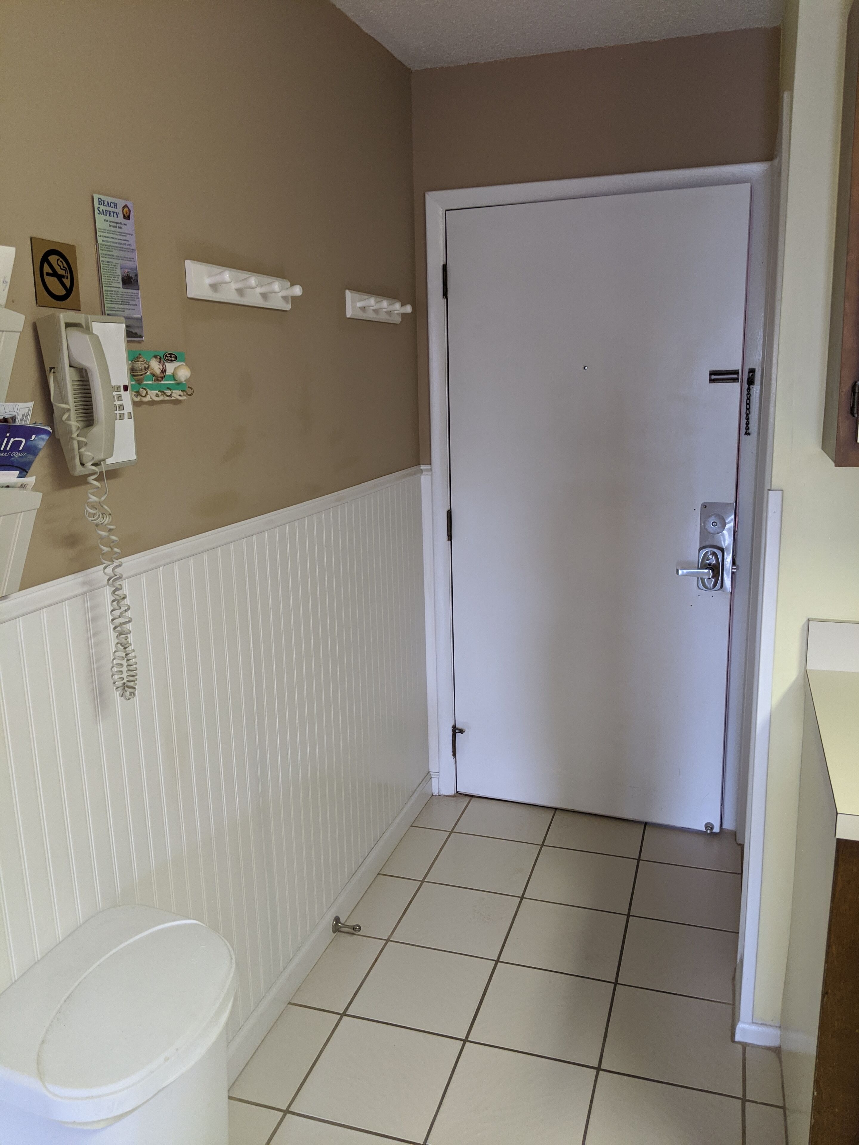 A narrow hallway with a white door, a telephone, and a trash bin.