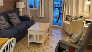 Una sala de estar acogedora con un sofá, una mesa de centro, una silla y vistas a un balcón con cortinas.