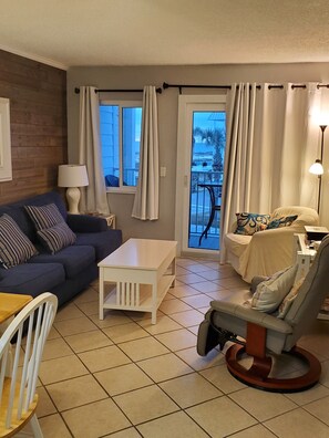 Relax in this stylish living area with a sofa, armchair, and coffee table, offering a view of palm trees and a building from the balcony.