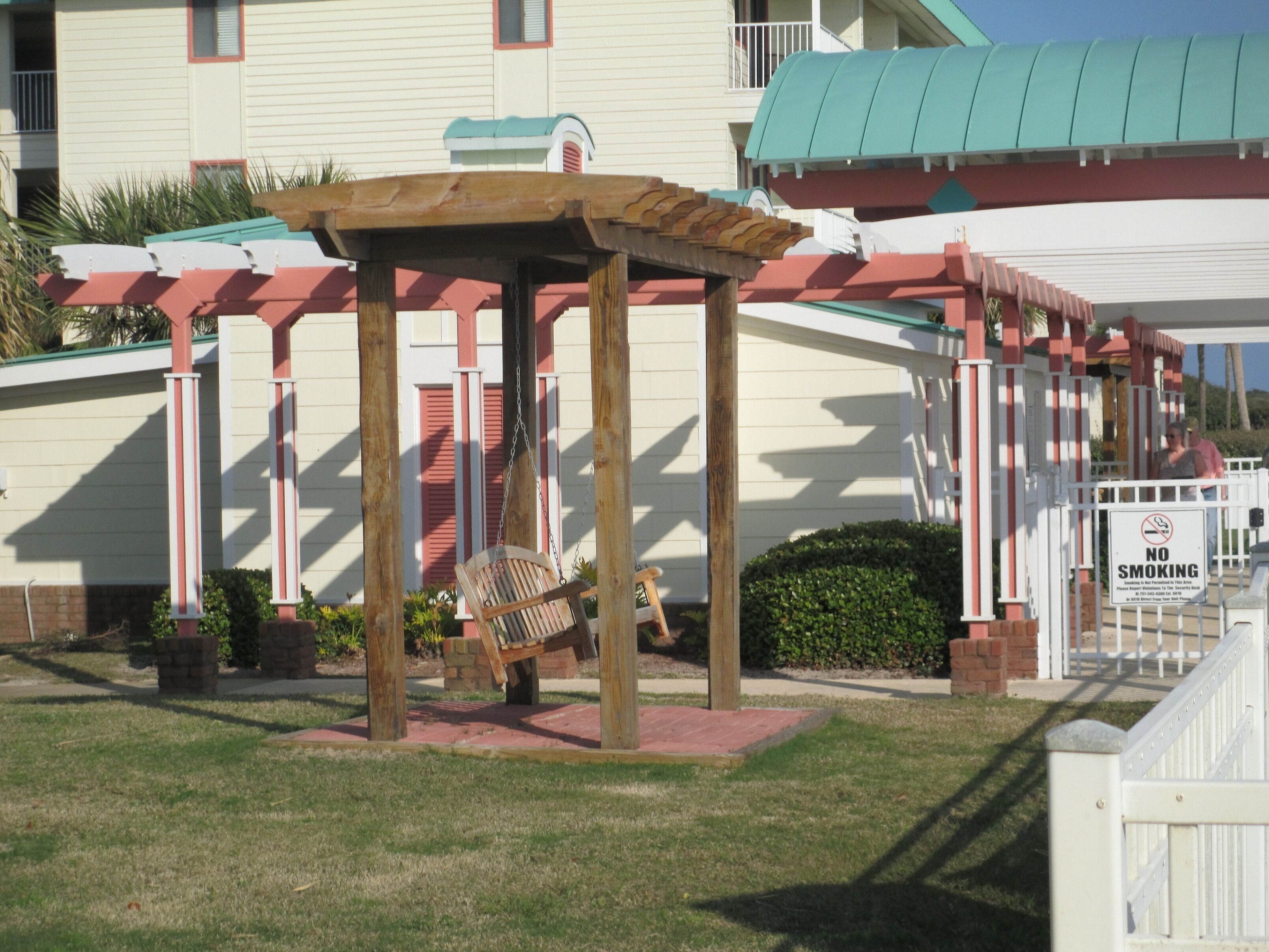 Eine Holz-Pergola mit Schaukelstuhl vor einem Gebäude mit einem Gründach und einem Rauchverbot-Schild.