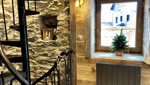 A rustic interior with a stone wall, a wooden staircase, a small Christmas tree, and a window with a view of a building. - Charming individual chalet (tignes les brevieres)