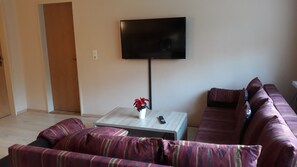 Ein Wohnzimmer mit einer Couch, einem Couchtisch, einem Fernseher und einer Tür.