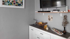 Ein modernes Wohnzimmer mit einem an der Wand befestigten Flachbildfernseher, einem gerahmten abstrakten Gemälde, einem dekorativen Korb und einem kleinen Beistelltisch mit Snacks.