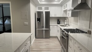 Uma cozinha moderna com eletrodomésticos de aço inoxidável, armários brancos e piso de madeira clara.