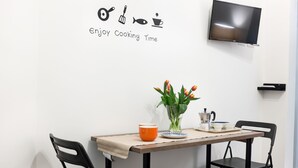 A dining area with a table set for two, a TV mounted on the wall, and a wall decoration with cooking utensils and the phrase "Enjoy Cooking Time". - Manuela Apartments 1 Piazza del Plebiscito - Centro (Napoli)