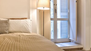 A bedroom with a bed, a floor lamp, a window with blinds, and a view of the outside. - Manuela Apartments 1 Piazza del Plebiscito - Centro (Napoli)