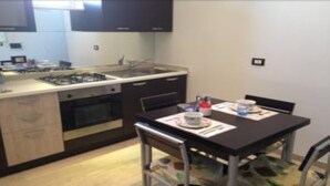 Cocina compacta con estufa a gas, horno y pileta, una pequeña mesa de comedor con sillas y un microondas.
