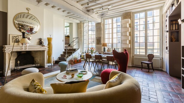 A spacious living room with a fireplace, comfortable seating, a dining area, and large windows providing natural light. - Beautiful Loft on Rue Quincampoix, by Veeve (Paris)