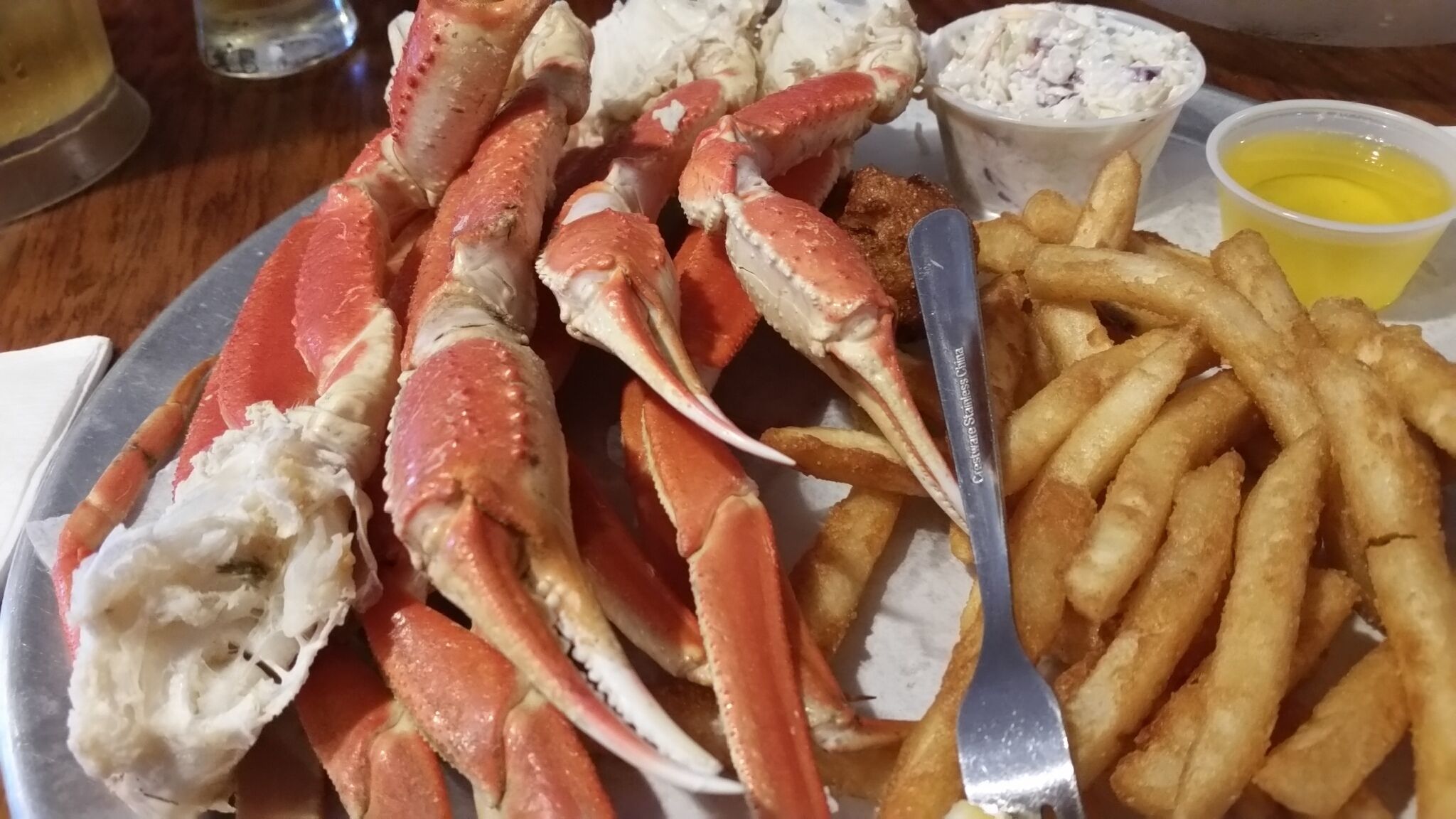 Une assiette de pattes de crabe, une fourchette, une portion de salade de chou et un récipient de sauce.