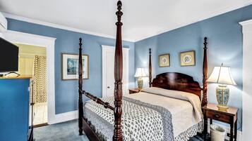 A bedroom with a four-poster bed, a bedside table with a lamp, a trash can, and a dresser.