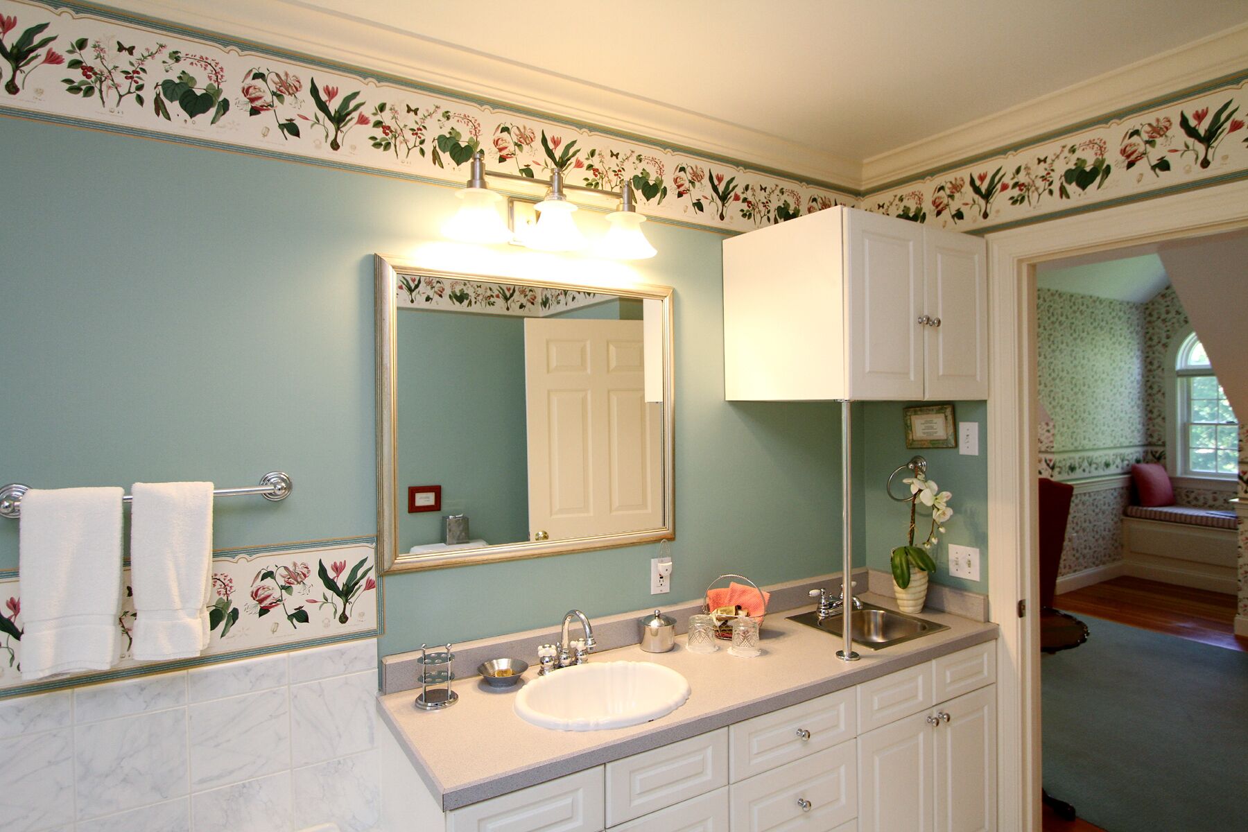 A bathroom with a floral wallpaper design, a large mirror, a sink, and a cabinet.