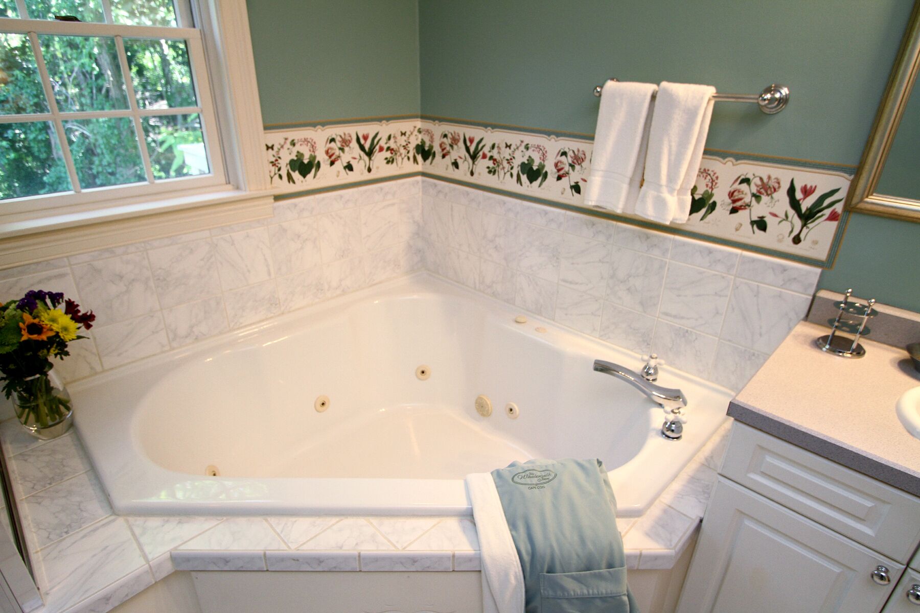 Un baño con una bañera grande, una ventana con vistas a árboles y un borde floral en la pared.
