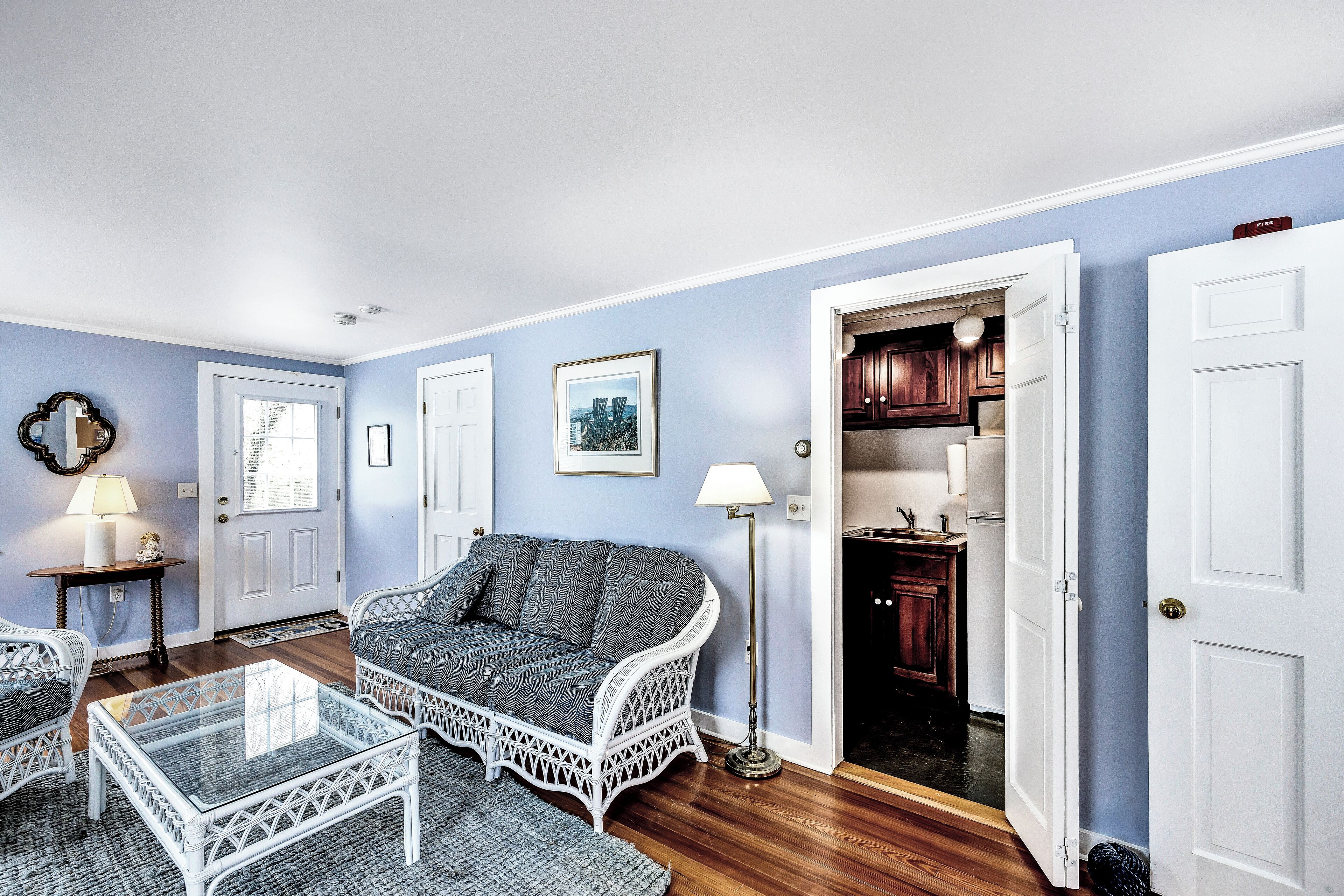 A living room with a grey sofa, white wicker furniture, and a glass coffee table.