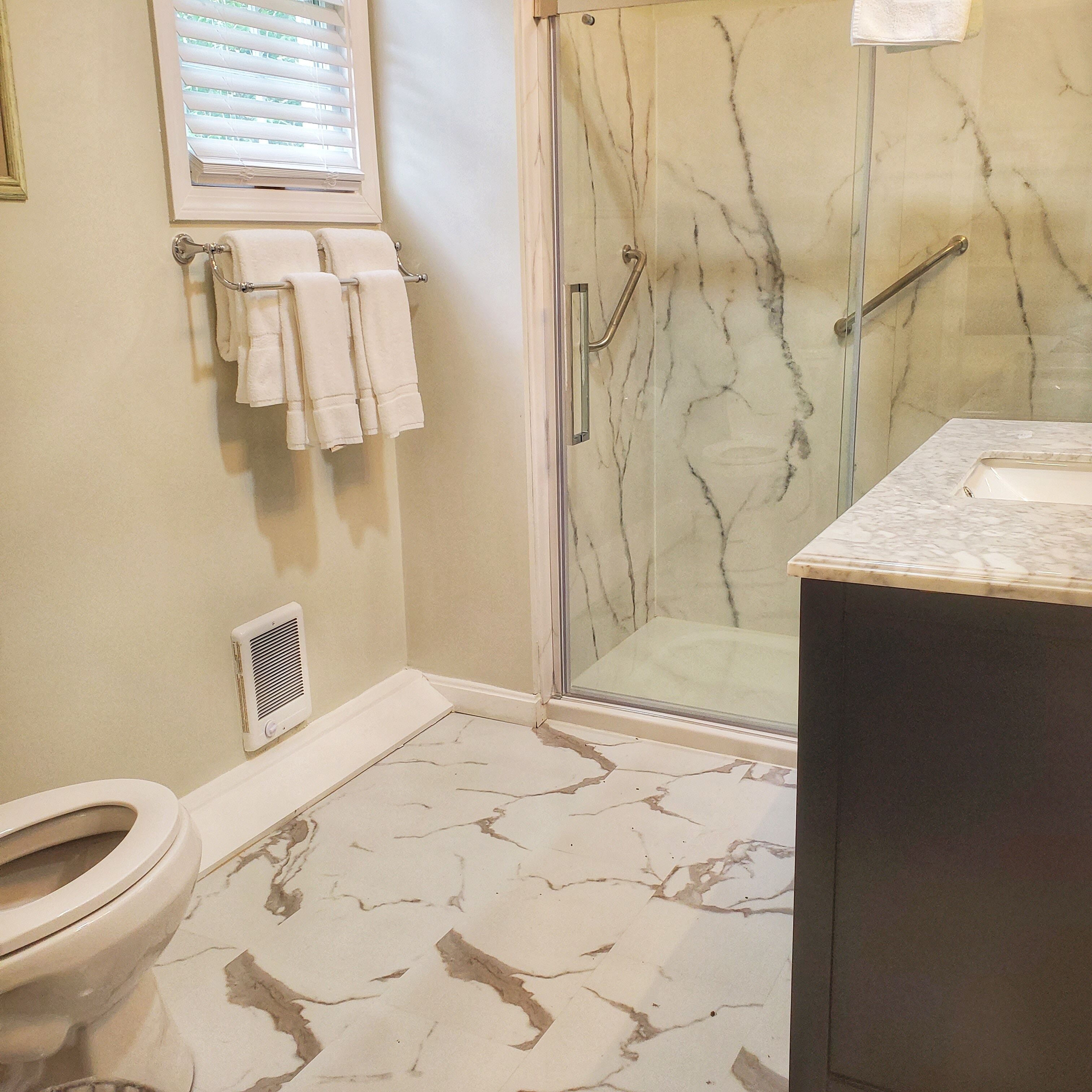 A bathroom with a glass shower enclosure, a toilet, and a sink with a marble countertop.