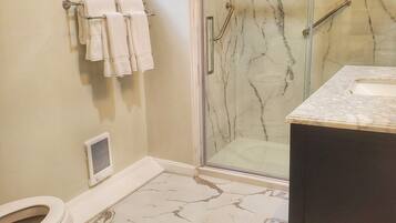 A bathroom with a glass shower enclosure, a toilet, and a sink with a marble countertop.