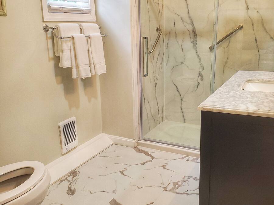 A bathroom with a glass shower enclosure, a toilet, and a sink with a marble countertop.