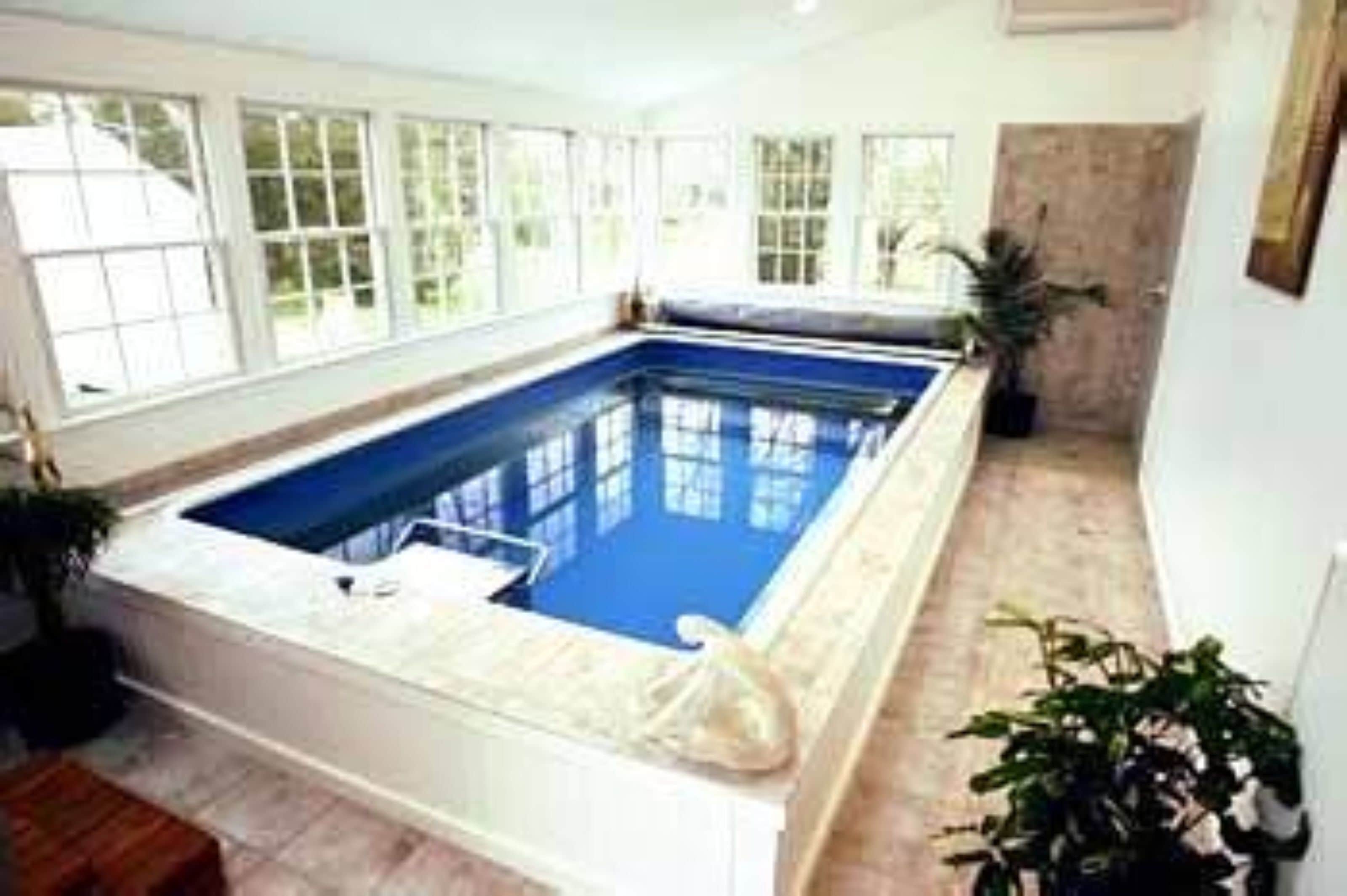A rectangular indoor swimming pool with clear blue water, surrounded by white walls and large windows.