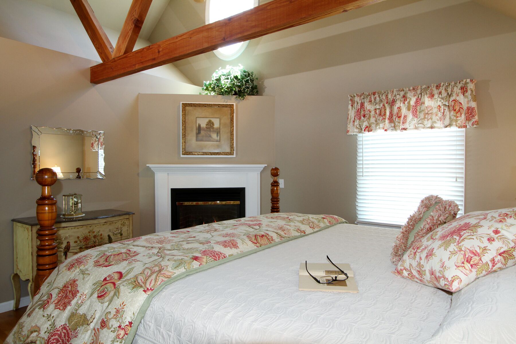 A bedroom with a bed, a dresser, a mirror, a fireplace, and a window with curtains.