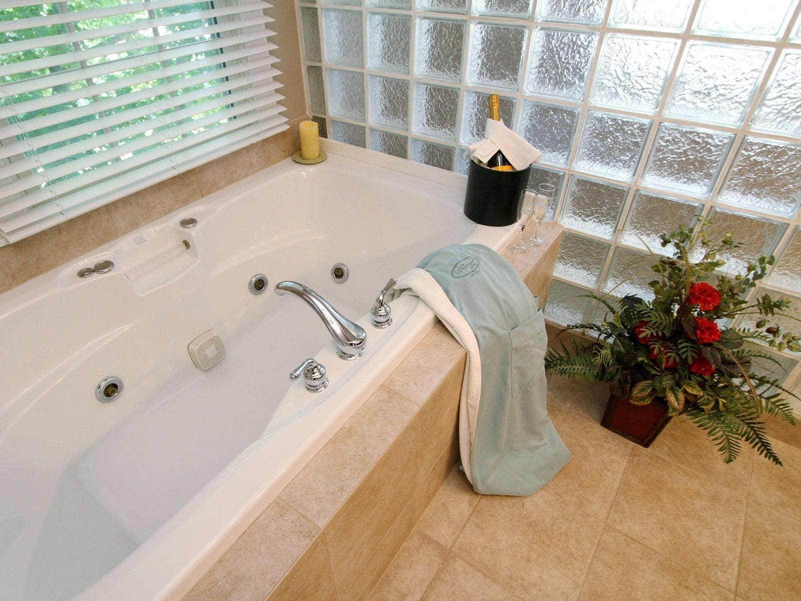 A bathroom with a large bathtub, a window with frosted glass, and a potted plant with red flowers.
