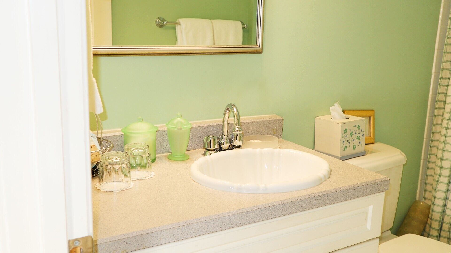 Un baño con un lavabo blanco, pared verde y un espejo sobre el lavabo.