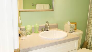 Un baño con un lavabo blanco, pared verde y un espejo sobre el lavabo.