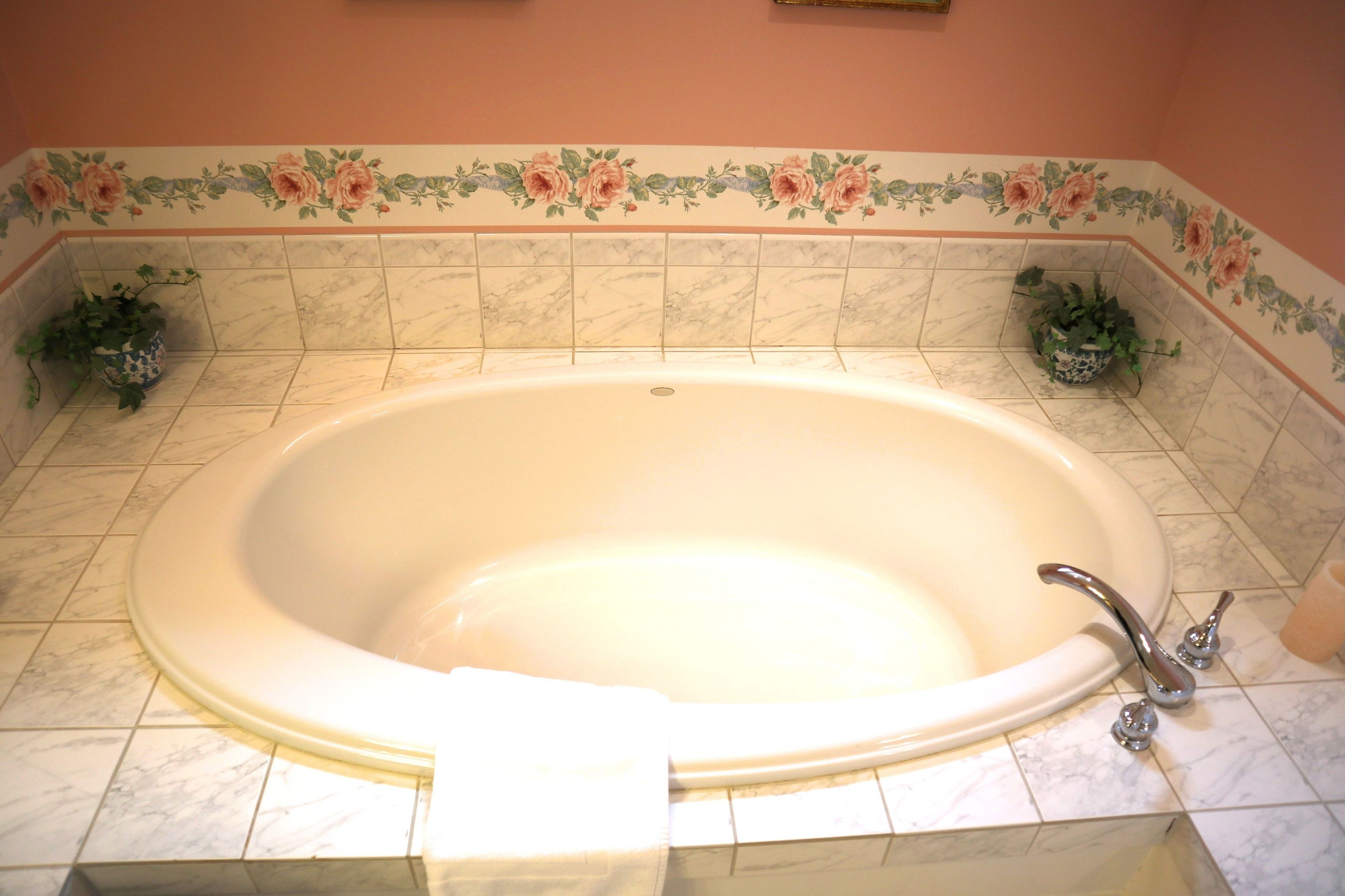 A large, oval-shaped bathtub with a single faucet, surrounded by a floral border on the wall.