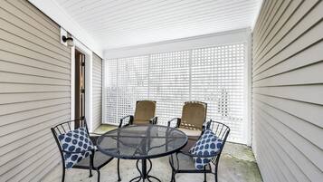 Un patio cubierto con una mesa redonda y cuatro sillas, una valla blanca y una puerta.
