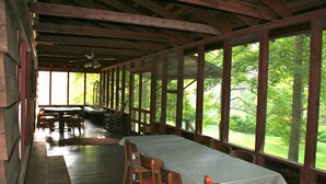 A covered dining area with wooden tables and chairs, large windows, and a view of the outdoors. - Large SECLUDED RIVERFRONT Cabin with PRIVATE access to CANOE/KAYAK Blue River (Depauw)