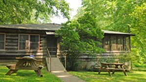 A rustic cabin with a wooden exterior, a porch, and a picnic table. - Large SECLUDED RIVERFRONT Cabin with PRIVATE access to CANOE/KAYAK Blue River (Depauw)