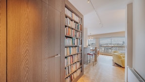 Un vaste espace de vie comprenant une grande bibliothèque en bois, un coin repas avec des chaises et une vue sur la ville grâce à de grandes fenêtres.