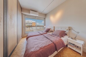A bedroom with a large bed, a bedside table with a lamp, and a view of the outside.