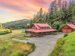 A two-story wooden cabin with a red roof, a covered porch, and a separate garage. - Custom built home on 5 private acres, unobstructed views, and a hot tub.  (Leavenworth)
