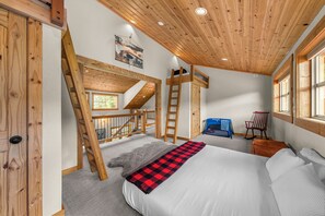 A bedroom with a bunk bed, a ladder, a desk, a chair, and a window.