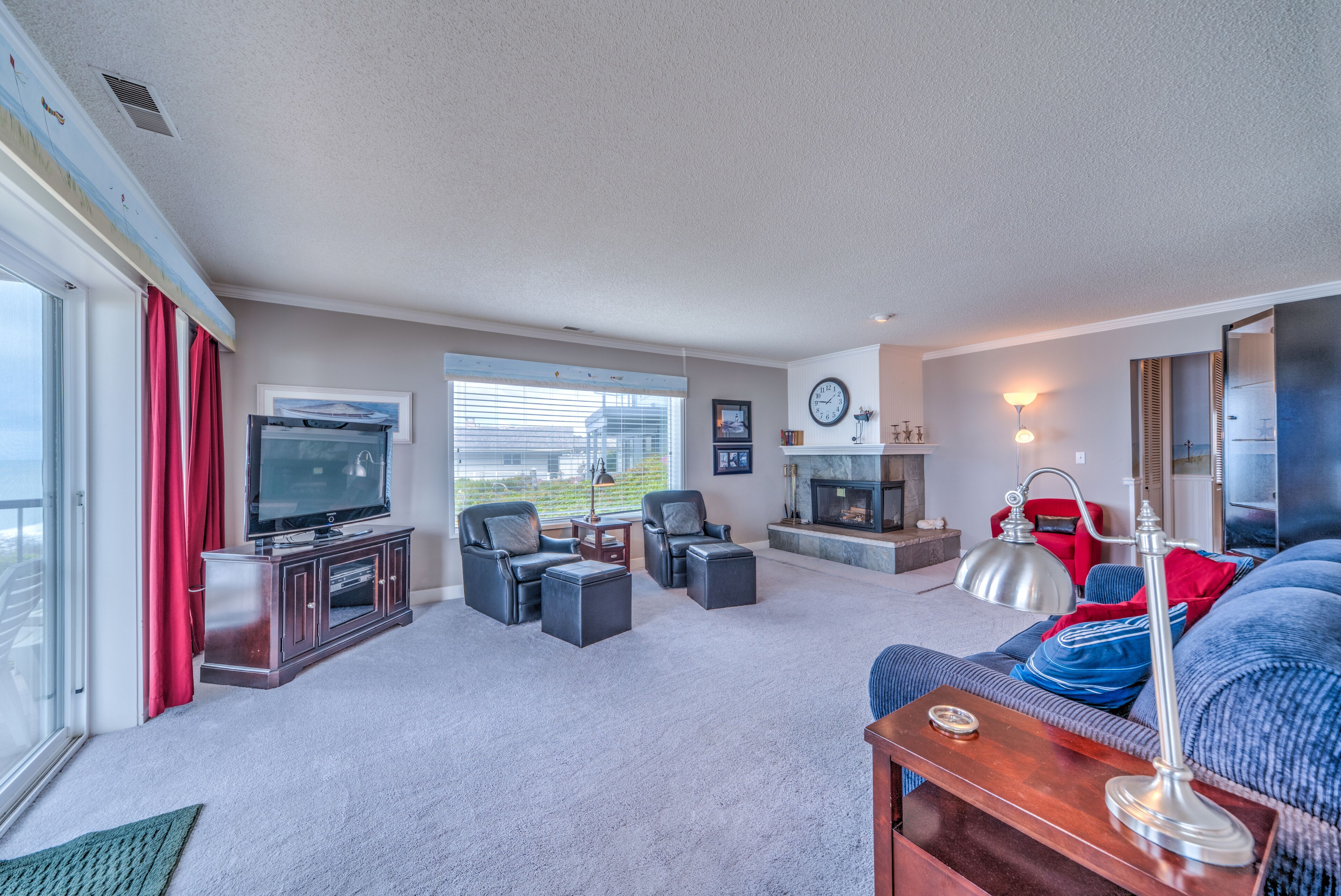 A spacious living room with a large TV, comfortable seating, a fireplace, and a view through the large window.